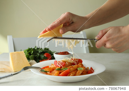 Woman rubs cheese on pasta with tomato sauce 78067948