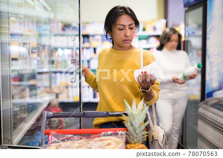Latina choosing dairy products in fridge at grocery store 78070563