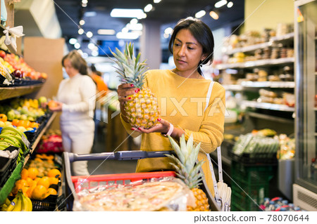 Woman picking ripe pineapple at supermarket Woman picking ripe pineapple at supermarket 78070644