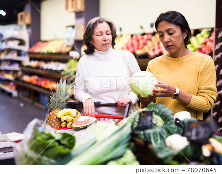 Two women helping each friend pick ripe cabbage at grocery supermarket Two women helping each friend pick ripe cabbage at grocery supermarket 78070645