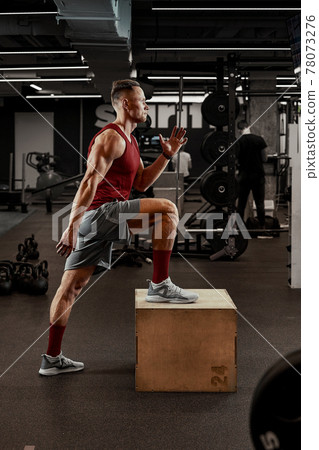 Sexy muscular men using the platform for his legs on a dark colorful background of gym. Sexy muscular men using the platform for his legs on a dark colorful background of gym. 78073276