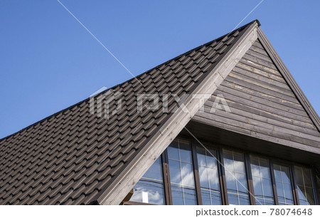 Brown corrugated metal profile roof installed on a modern house. The roof of corrugated sheet. Roofing of metal profile wavy shape. Modern roof made of metal. Metal roofing. Brown corrugated metal profile roof installed on a modern house. The roof of corrugated sheet. Roofing of metal profile wavy shape. Modern roof made of metal. Metal roofing. 78074648