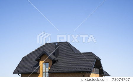 Brown corrugated metal profile roof installed on a modern house with a attic windows. The roof of corrugated sheet. Roofing of metal profile wavy shape. Modern roof made of metal. Metal roofing. Brown corrugated metal profile roof installed on a modern house with a attic windows. The roof of corrugated sheet. Roofing of metal profile wavy shape. Modern roof made of metal. Metal roofing. 78074707