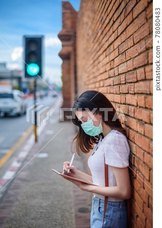 young working asian woman wear surgical mask with tablet at Thapae Gate landmark of Chiang Mai province, Thailand 78080483