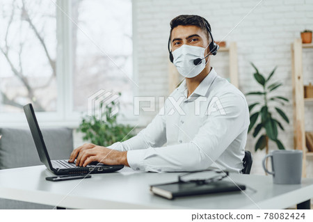 Young businessman sitting at his working desk with medical mask on Young businessman sitting at his working desk with medical mask on 78082424