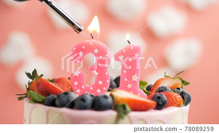 Birthday cake number 31, pink candle on beautiful cake with berries and lighter with fire against background of white clouds and pink sky. Close-up Birthday cake number 31, pink candle on beautiful cake with berries and lighter with fire against background of white clouds and pink sky. Close-up 78089259