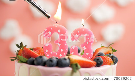 Birthday cake number 33, pink candle on beautiful cake with berries and lighter with fire against background of white clouds and pink sky. Close-up Birthday cake number 33, pink candle on beautiful cake with berries and lighter with fire against background of white clouds and pink sky. Close-up 78089262
