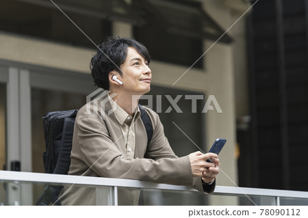 A man in his early 30s wearing headphones and holding a smartphone A man in his early 30s wearing headphones and holding a smartphone 78090112