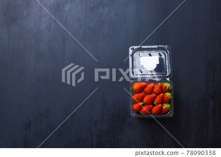 Picture of a box of fresh red strawberry. The strawberry come with green leaves. The box is a clear plastic box. It is placed on a black wooden table. Picture of a box of fresh red strawberry. The strawberry come with green leaves. The box is a clear plastic box. It is placed on a black wooden table. 78090338