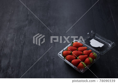 Picture of a box of fresh red strawberry. The strawberry come with green leaves. The box is a clear plastic box. It is placed on a black wooden table. Picture of a box of fresh red strawberry. The strawberry come with green leaves. The box is a clear plastic box. It is placed on a black wooden table. 78090339