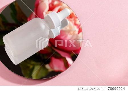 Glass bottle with oil on round mirror on pink background Glass bottle with oil on round mirror on pink background 78090924