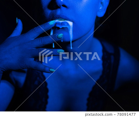 A thick white liquid flows down the lips of a young European girl. Dripping down. Ultraviolet, blue light. Close-up portrait. Spit out. A thick white liquid flows down the lips of a young European girl. Dripping down. Ultraviolet, blue light. Close-up portrait. Spit out. 78091477
