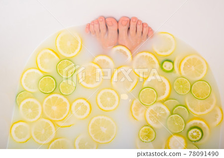 Girl takes a milk bath with lemons and limes. Citrus spa. Body care. Skin whitening. Women's feet. 78091490
