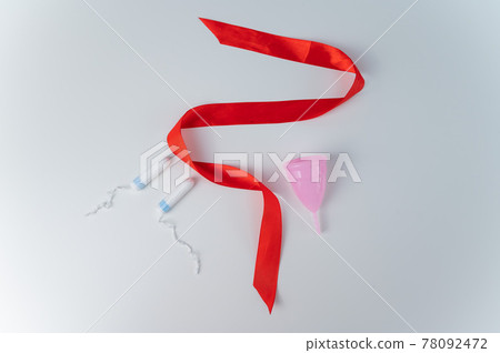 Tampon, pink menstrual cup and red satin ribbon on a white background. Means of intimate hygiene of a woman during mentruation Tampon, pink menstrual cup and red satin ribbon on a white background. Means of intimate hygiene of a woman during mentruation 78092472