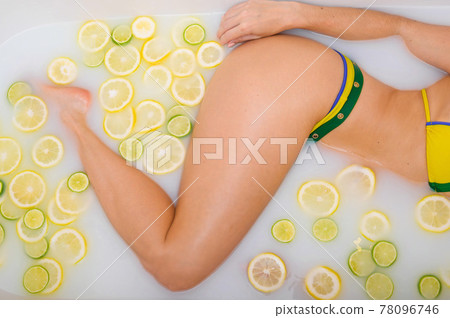 Beautiful Unrecognizable woman takes a milk bath with lemon and lime slices. Skin care and whitening. A girl in a yellow-green bikini does the Cleopatra rejuvenation procedure. Beautiful Unrecognizable woman takes a milk bath with lemon and lime slices. Skin care and whitening. A girl in a yellow-green bikini does the Cleopatra rejuvenation procedure. 78096746