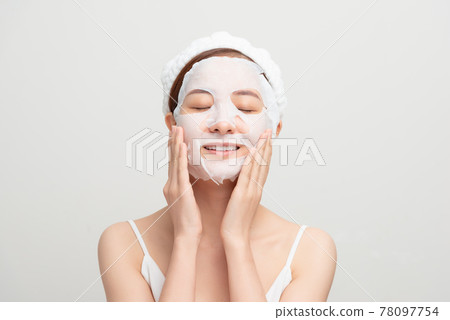 Closeup portrait of young pretty woman applying paper sheet mask on her face. Cosmetic procedure. Beauty spa and cosmetology. 78097754