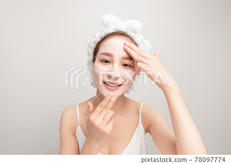 Young woman applying moisturizer cream on her face. Photo of smiling woman receiving spa treatments. Grooming himself 78097774