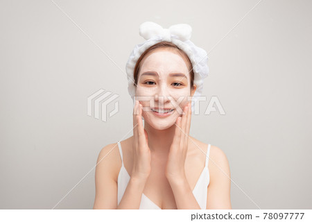 Portrait of confident lady in bathrobe and towel on head with joy while touching her face with clay mask while using anti-aging procedures 78097777