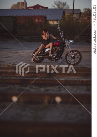 Beautiful sexy woman in lace bodysuit and high heels sits on a motorcycle on an industrial background 78102103