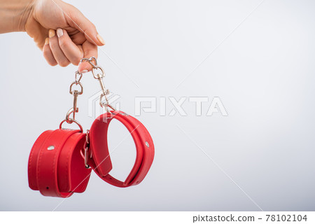 Red leather handcuffs in female hands on a white background. BDSM accessories 78102104
