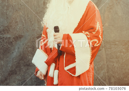 The actor dressed as Santa Claus performs on stage with a microphone against a black background. 78103076