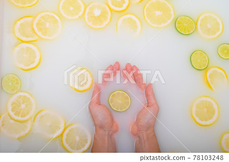 A slice of ripe lime in the hands of a woman. Top view Girl takes a milk bath with lemons. Citrus spa. A slice of ripe lime in the hands of a woman. Top view Girl takes a milk bath with lemons. Citrus spa. 78103248