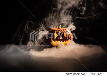 Halloween, orange pumpkin with a scary luminous face on a dark background. Thick gray smoke comes out and spreads across the black table. A close-up of a flashlight on the eve of all the saints Halloween, orange pumpkin with a scary luminous face on a dark background. Thick gray smoke comes out and spreads across the black table. A close-up of a flashlight on the eve of all the saints 78103249