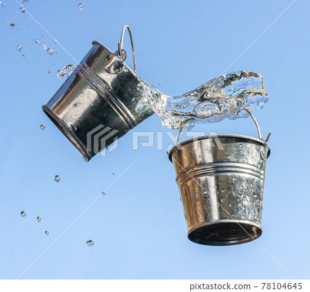 A pouring water from falling bucket to bucket, on a background of blue sky. A pouring water from falling bucket to bucket, on a background of blue sky. 78104645