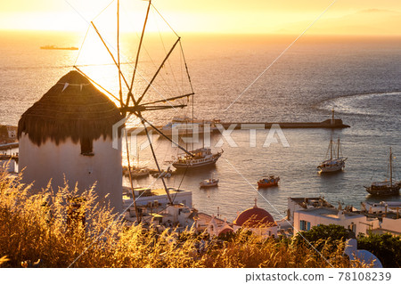 Golden sunset over sea horizon in Mykonos, Greece. Famous traditional white windmill on hot summer evening in sunlight. Romantic travel destinations 78108239