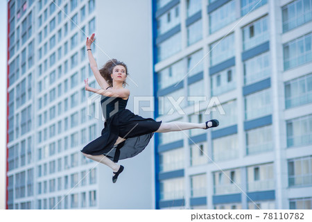 Ballerina in a tutu posing at a multi-storey residential building. Beautiful young woman in black dress and pointe shoes outside. Gorgeous ballerina performs elegant jumps. Ballerina in a tutu posing at a multi-storey residential building. Beautiful young woman in black dress and pointe shoes outside. Gorgeous ballerina performs elegant jumps. 78110782