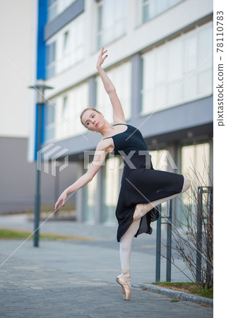 Ballerina in a tutu posing against the backdrop of a residential building. Beautiful young woman in black dress and pointe shoes dancing ballet outside. Ballerina in a tutu posing against the backdrop of a residential building. Beautiful young woman in black dress and pointe shoes dancing ballet outside. 78110783
