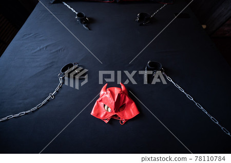 BDSM equipment. Top view of a red leather devil mask and black handcuffs with chains on a gray sheet. Sex toys. Dominance. No people. BDSM equipment. Top view of a red leather devil mask and black handcuffs with chains on a gray sheet. Sex toys. Dominance. No people. 78110784