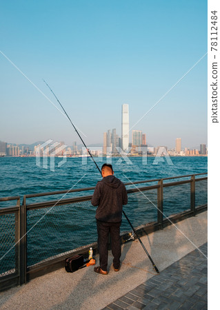 fisher man with fishing rod on coast with skyline of Hong Kong, Kowloon fisher man with fishing rod on coast with skyline of Hong Kong, Kowloon 78112484