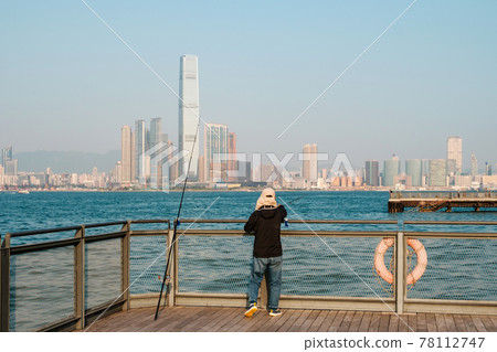 fisher man with fishing rod on coast with HongKong skyline fisher man with fishing rod on coast with HongKong skyline 78112747