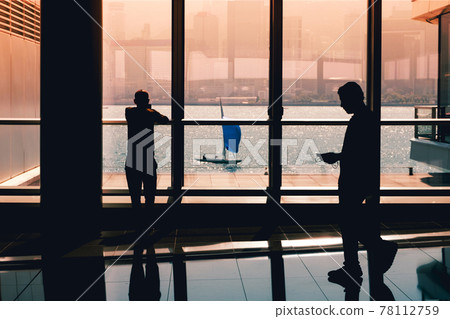 business people looking on mobile phone inside office building with ocean view window and sailing boat 78112759