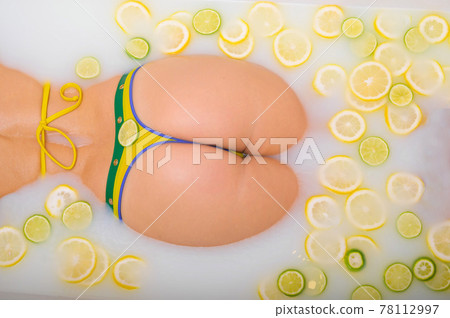 Beautiful woman takes a milk bath with lemon and lime slices. Skin Care & Whitening. Unrecognizable Girl in a Yellow-Green Bikini 78112997