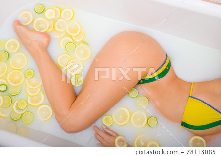 Beautiful woman takes a milk bath with lemon and lime slices. Skin Care and Whitening. Unrecognizable Girl in a Yellow-Green Bikini Beautiful woman takes a milk bath with lemon and lime slices. Skin Care and Whitening. Unrecognizable Girl in a Yellow-Green Bikini 78113085