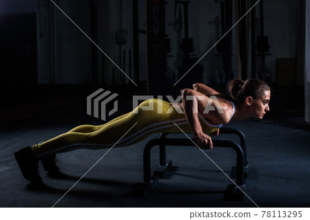 Young athletic girl in yellow tight sports uniform doing horizontal push-ups with bars in gym Young athletic girl in yellow tight sports uniform doing horizontal push-ups with bars in gym 78113295