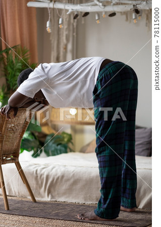 African young man working out, practicing yoga, standing in Ardha Uttanasana 78115000
