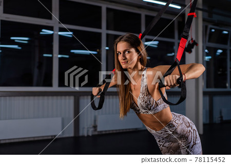 Beautiful young sportswoman is doing exercises with equipment. A woman in the gym for circular training is engaged in loops TRX. Athlete Making Functional workout With Suspension Cable. straps system. 78115452