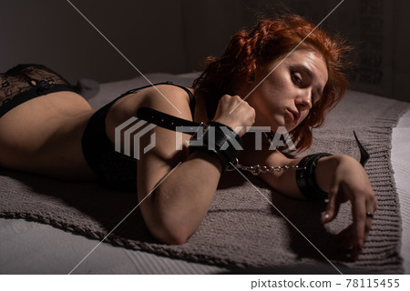 A young girl in sexy lingerie, lying on the bed handcuffed. BDSM games and entertainment. Sexual perversion. 78115455