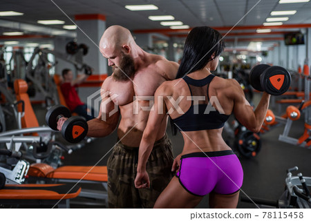 Powerful, muscular, strong, man and woman, pick up the dumbbell with your hands. Nice bicep. They look in different directions. Sports hall 78115458