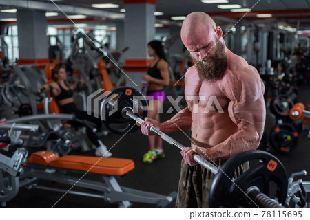 Bald man with a beard in the gym. Muscular bodybuilder guy doing barbell exercises. Strong man with a naked torso. The young athlete is preparing for weightlifting competitions. Bald man with a beard in the gym. Muscular bodybuilder guy doing barbell exercises. Strong man with a naked torso. The young athlete is preparing for weightlifting competitions. 78115695