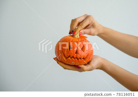 Female hands holding a pumpkin for Halloween. Close-up of a woman opens the jack-o'-lantern cover on a white background on the eve of all the saints. front view. 78116051