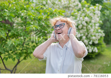 Happy old woman in headphones and dancing and singing in a park of blooming apple trees. An active female pensioner is enjoying a warm summer day. Grandma listens to music on a smartphone. Happy old woman in headphones and dancing and singing in a park of blooming apple trees. An active female pensioner is enjoying a warm summer day. Grandma listens to music on a smartphone. 78116053