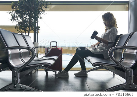 woman traveler with baggage sits in the waiting room of the airport and is waiting for the flight woman traveler with baggage sits in the waiting room of the airport and is waiting for the flight 78116665