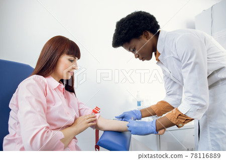 Preparation for blood test. Beautiful young African woman doctor in white medical uniform ready to take blood sample from patient's vein. Preparation for blood test. Beautiful young African woman doctor in white medical uniform ready to take blood sample from patient's vein. 78116889