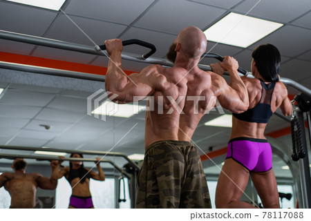 Powerful, muscular, strong, guy and girl, train back. together are tightened on a horizontal bar. Sports hall 78117088