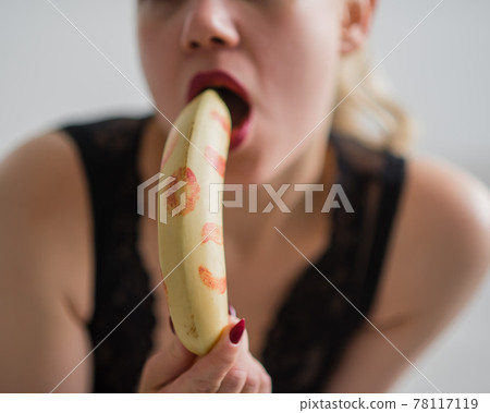 Woman with sensual red lips sucks and licks a banana. Unrecognizable blonde fantasizes about blowjob. Close-up of a female mouth. Woman with sensual red lips sucks and licks a banana. Unrecognizable blonde fantasizes about blowjob. Close-up of a female mouth. 78117119