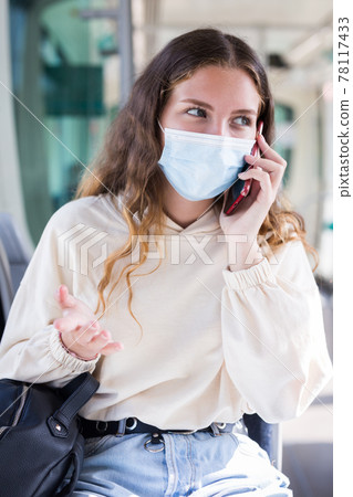 Woman in mask using mobile phone on way to work in tram Woman in mask using mobile phone on way to work in tram 78117433